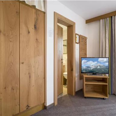 A cozy room with a wooden wardrobe and a television. The bathroom is visible through the door on the right side.