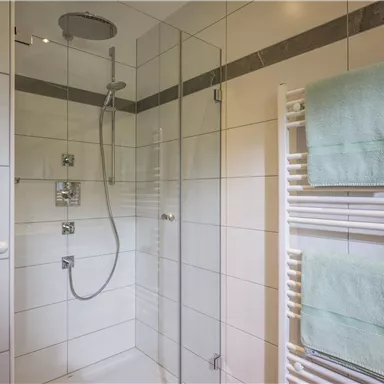 A modern shower cabin with transparent walls and bright tiles. Two green towels hang on a towel holder.