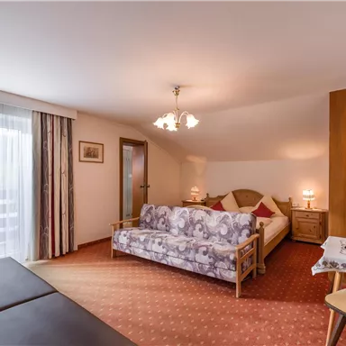 A cozy bedroom with a double bed and a sofa bed. Bright curtains and a warm color scheme create an inviting atmosphere.