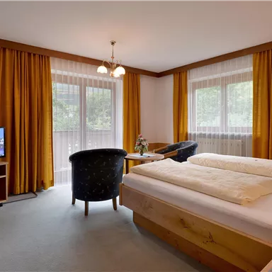 A cozy hotel room with two beds and a sitting area. Large windows let in plenty of light, and a TV is also available.