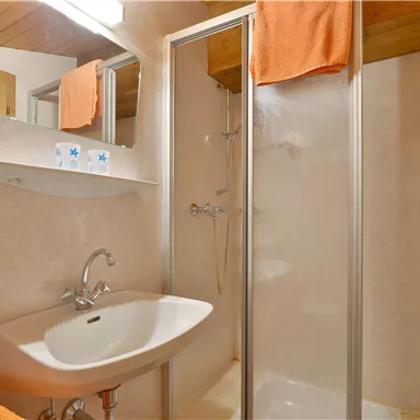 A bright bathroom with a shower, sink, and large mirrors. Orange towels hang on the wall.