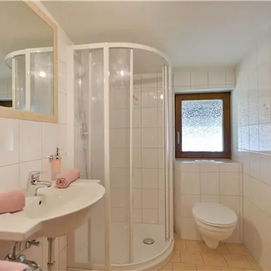 A modern bathroom with a shower cubicle, a sink, and a toilet. The walls are brightly tiled, and there are towels in gentle colors.