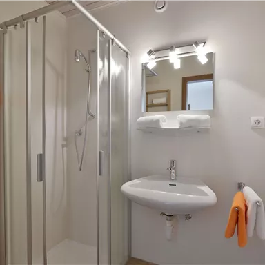 Ein modernes Badezimmer mit einer Duschkabine und einem Waschbecken. Handtücher in Orange verleihen dem Raum einen frischen Akzent.