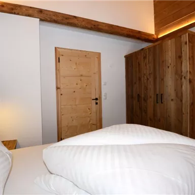 Ein gemütliches Schlafzimmer mit einem Holzschrank und einem Fernseher. Die Bettwäsche ist weiß und sauber, und das Licht ist entspannend.