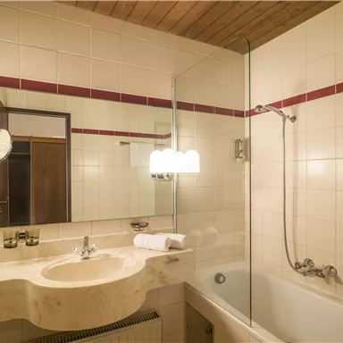 Ein modernes Badezimmer mit einer Badewanne und einer separaten Dusche. Der Raum hat helle Fliesen und eine Holzdecke.