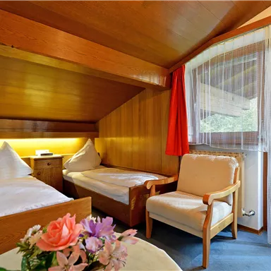 A cozy room with two single beds and a comfortable armchair. Large windows let in plenty of light and offer a view outside.