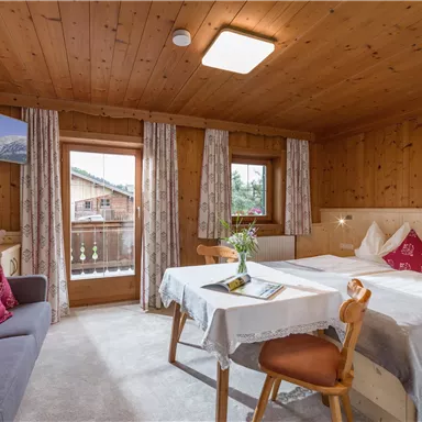Ein gemütliches Zimmer mit Holzdecke und zwei Betten. Es gibt einen kleinen Tisch, einen Fernseher und Fenster mit Blick nach draußen.