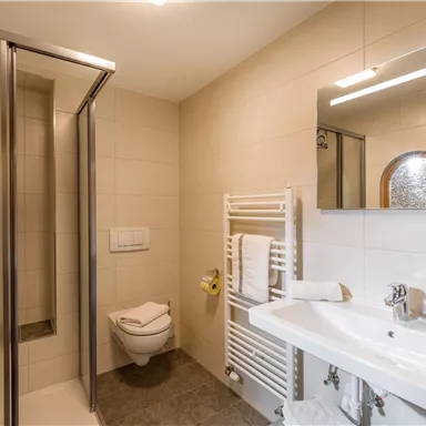 Ein modernes Badezimmer mit Dusche, Waschbecken und großen Spiegel. Saubere Fliesen und Handtücher sorgen für eine einladende Atmosphäre.