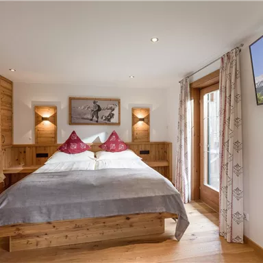 Ein gemütliches Schlafzimmer mit einem Holzbett und dekorativen Kissen. Große Fenster lassen viel Licht herein und bieten einen schönen Blick auf die Umgebung.