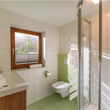 Ein modernes Badezimmer mit einer Dusche und einem Fenster. Die Wände sind hell gefliest, und es gibt farbige Akzente in grün.