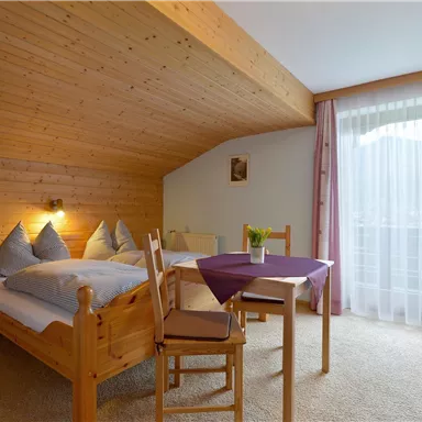 A cozy bedroom with wood paneling and two beds. A small table by the window with a view outside.