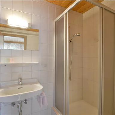 Ein modernes Badezimmer mit einer Dusche und einem Waschbecken. Es ist hell und sauber mit weißen Fliesen.