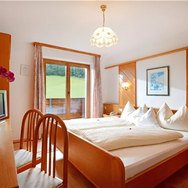A cozy room with two beds and wooden interiors. Large windows offer a view of the greenery.