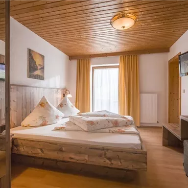 Ein gemütliches Schlafzimmer mit einem großen Bett und Holzmöbeln. Der Raum hat Fenster mit Vorhängen und einen Schreibtisch aus Holz.