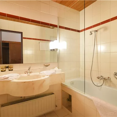 Ein modernes Badezimmer mit einer Badewanne und einem Waschbecken. Die Wände sind hell gefliest, und es gibt eine große Spiegeloberfläche.