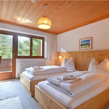 Ein gemütliches Schlafzimmer mit zwei Einzelbetten aus Holz. Der Raum hat große Fenster, die viel Tageslicht hereinlassen.