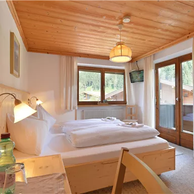 Ein gemütliches Schlafzimmer mit Holzdekor, einem Doppelbett und großen Fenstern. Es gibt einen Fernseher und einen Balkon mit Blick auf die Umgebung.