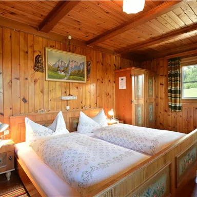 A cozy bedroom with wooden walls and a double bed. There is a pleasant atmosphere with windows that let in daylight.