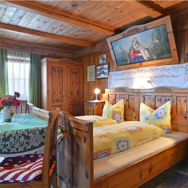 A cozy room with wooden walls and a large bed. There is a flower vase on the table and a painting on the wall.