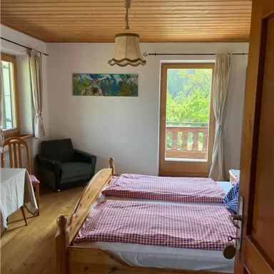 Ein gemütliches Schlafzimmer mit zwei Betten und einem Sessel. Das Fenster bietet einen Blick auf die Natur draußen.