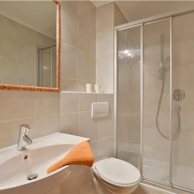 A modern bathroom with a shower and a sink. Towels in orange provide a colorful accent.