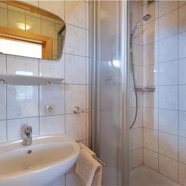 Ein modernes Badezimmer mit einer Duschkabine und einem Waschbecken. Die Wände sind mit weißen Fliesen gefliest und es gibt ein Wandspiegel.