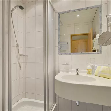 A modern bathroom with a shower and a sink. The walls are tiled in light colors, and a mirror reflects the space.