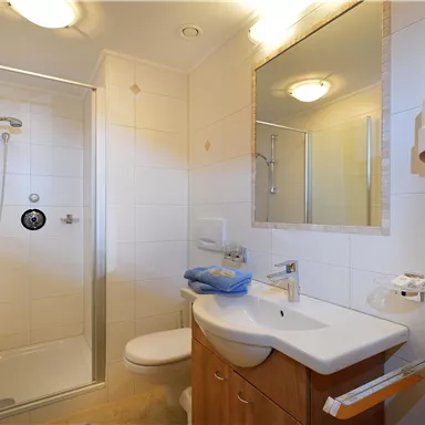 Ein modernes Badezimmer mit einer Dusche, Waschbecken und WC. Die Wände sind hell gefliest und es gibt einen großen Spiegel.