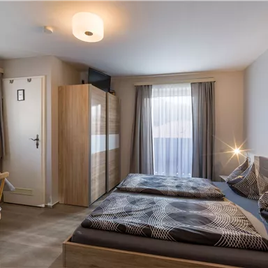 A modern room with two single beds and a table. Large windows provide plenty of daylight and a pleasant atmosphere.