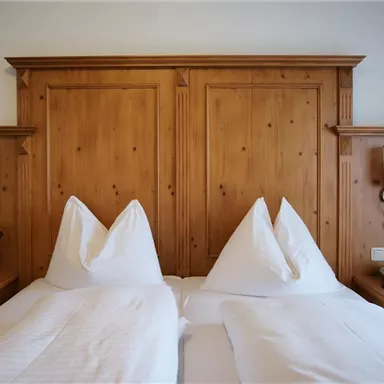 Ein gemütliches Schlafzimmer mit einem Doppelbett und zwei Kissen in Form von Hüten. Die Wände sind aus Holz, und es gibt Nachttische mit Lampen.