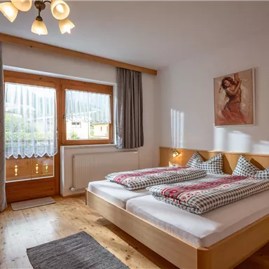 Ein gemütliches Schlafzimmer mit zwei Betten und karierten Kissen. Große Fenster sorgen für viel Licht und eine angenehme Atmosphäre.