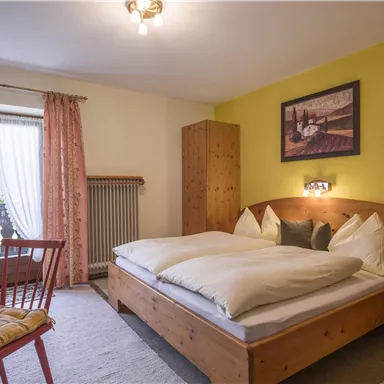 Ein gemütliches Schlafzimmer mit einem Doppelbett und Holzverkleidung. Der Raum hat große Fenster mit Vorhängen und einen kleinen Tisch mit Stühlen.