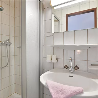 Ein modernes Badezimmer mit einer Dusche und einem Waschbecken. Die Wände sind gefliest und es gibt einen Spiegel über dem Waschbecken.