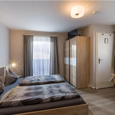 A modern room with two single beds, a desk, and a large window. The walls are light and the decor is simple and elegant.