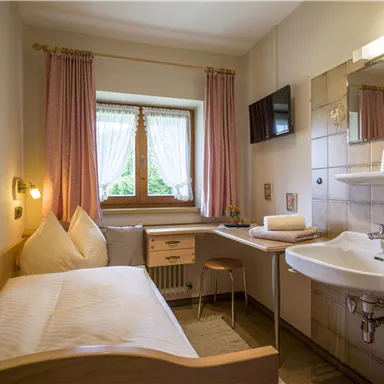 Ein kleines, gemütliches Zimmer mit einem Einzelbett und einem Tisch. Das Zimmer hat ein Fenster mit Blick ins Freie und eine moderne sanitäre Einrichtung.