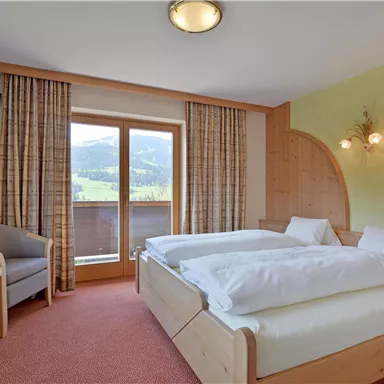 A cozy bedroom with two beds and a TV. Large windows offer a view of the mountains.