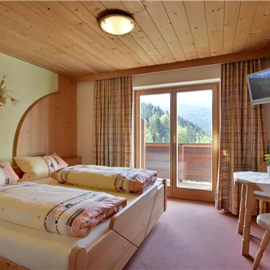 A cozy room with two beds and wooden paneling. It has a balcony with a view of the mountains and a television.