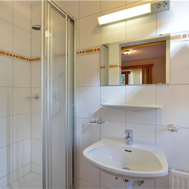 Ein modernes Badezimmer mit Dusche und Waschbecken. Die Wände sind hell gefliest und es gibt einen Spiegel über dem Waschbecken.