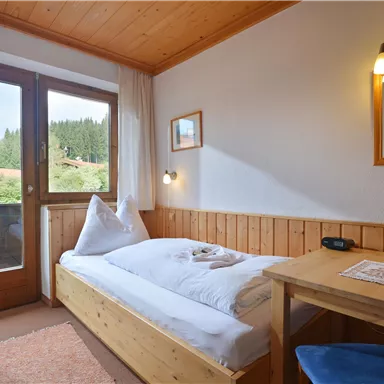 Ein gemütliches Zimmer mit einem Einzelbett und Holzverkleidung. Durch die Fenster gelangt viel Tageslicht und bietet einen Blick auf die Umgebung.