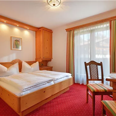 Ein gemütliches Schlafzimmer mit hellen Holzmöbeln und roten Teppich. Das Zimmer verfügt über ein großes Bett, einen Tisch und einen Fernseher sowie Fenster mit Vorhängen.