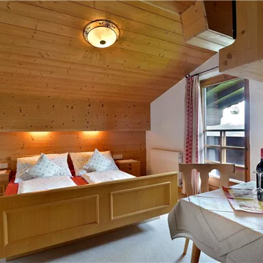 Ein gemütliches Zimmer mit Holzverkleidung und zwei Betten. Auf dem Tisch stehen eine Flasche Wein und eine Zeitschrift.