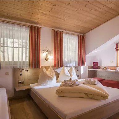 Ein gemütliches Zimmer mit hölzernem Boden und warmen Farben. Es ist hell erleuchtet und verfügt über große Fenster sowie ein bequemes Bett.