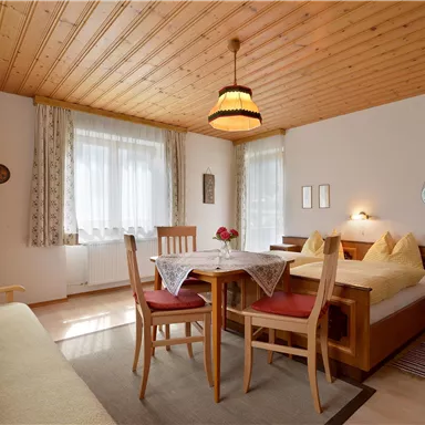 Eine gemütliche Wohnung mit Holzdecke und warmen Farben. Der Raum enthält einen Esstisch, Stühle und ein Bett mit dekorativen Kissen.