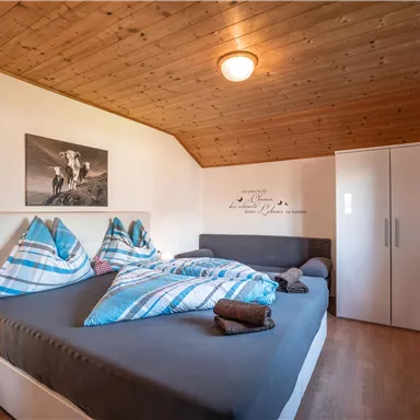 Ein gemütliches Schlafzimmer mit einem Doppelbett und hellen Bettdecken. Die Wände sind in sanften Farben gehalten und es gibt ein Fenster mit roten Vorhängen.