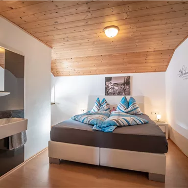 Ein gemütliches Schlafzimmer mit einem Doppelbett und Holzdecke. Das Zimmer ist modern eingerichtet und hat ein angrenzendes Badezimmer.