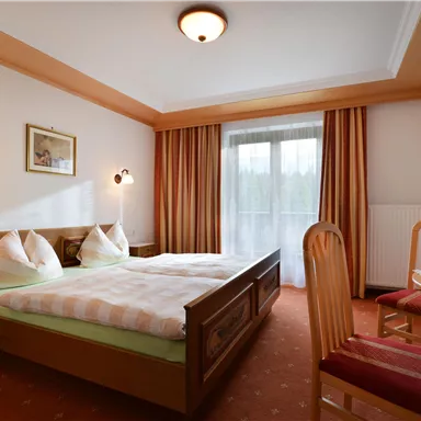 Ein gemütliches Schlafzimmer mit zwei Betten und einem kleinen Tisch. Das Zimmer hat große Fenster und warme, einladende Farben.