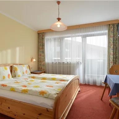 A cozy bedroom with two beds and colorful flower bedding. There is a table with a plant pot and a television on the wall.