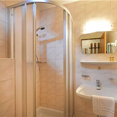 A modern bathroom with a shower cubicle and bright tiles. On the shelf, personal care products and a plant are visible.