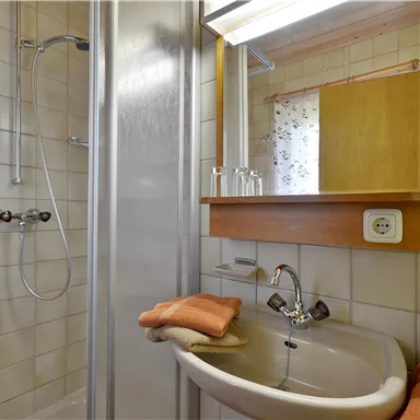 Ein kleiner, sauberer Badezimmerbereich mit einer Dusche und einem Waschbecken. Handtücher liegen bereit und ein Spiegel ist an der Wand angebracht.