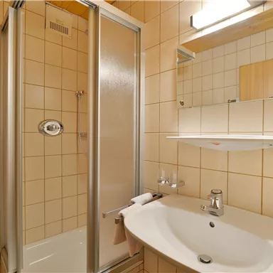A modern bathroom with a shower and a sink. The walls are tiled with bright tiles and a mirror hangs above the sink.